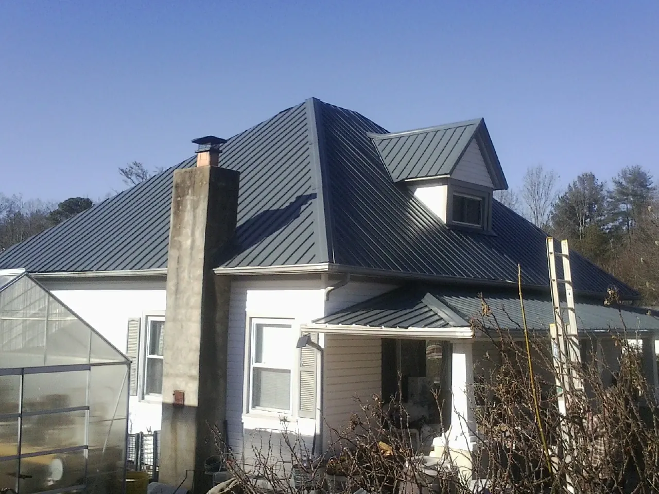 Dark blue standing seam metal roof on a white farmhouse with dormer — Slate & Tile Roof Repair by Roofing Brothers in Bentleyville