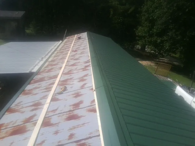 Old rusted panels beside newly installed green metal roofing — Wind Damage Roof Repair by Roofing Brothers in Bentleyville