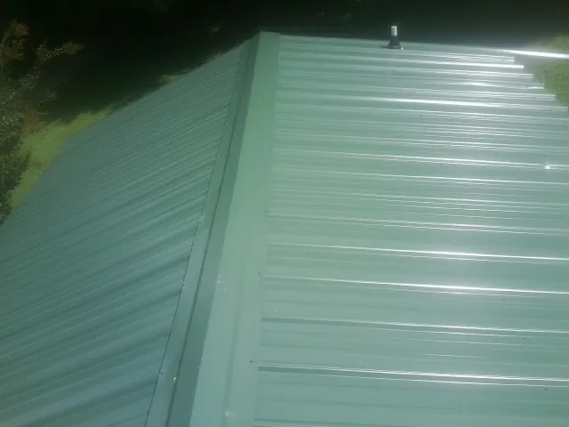 New green metal panels meeting at the ridge of a roof — Flat Roof Repair work by our crew in Bentleyville
