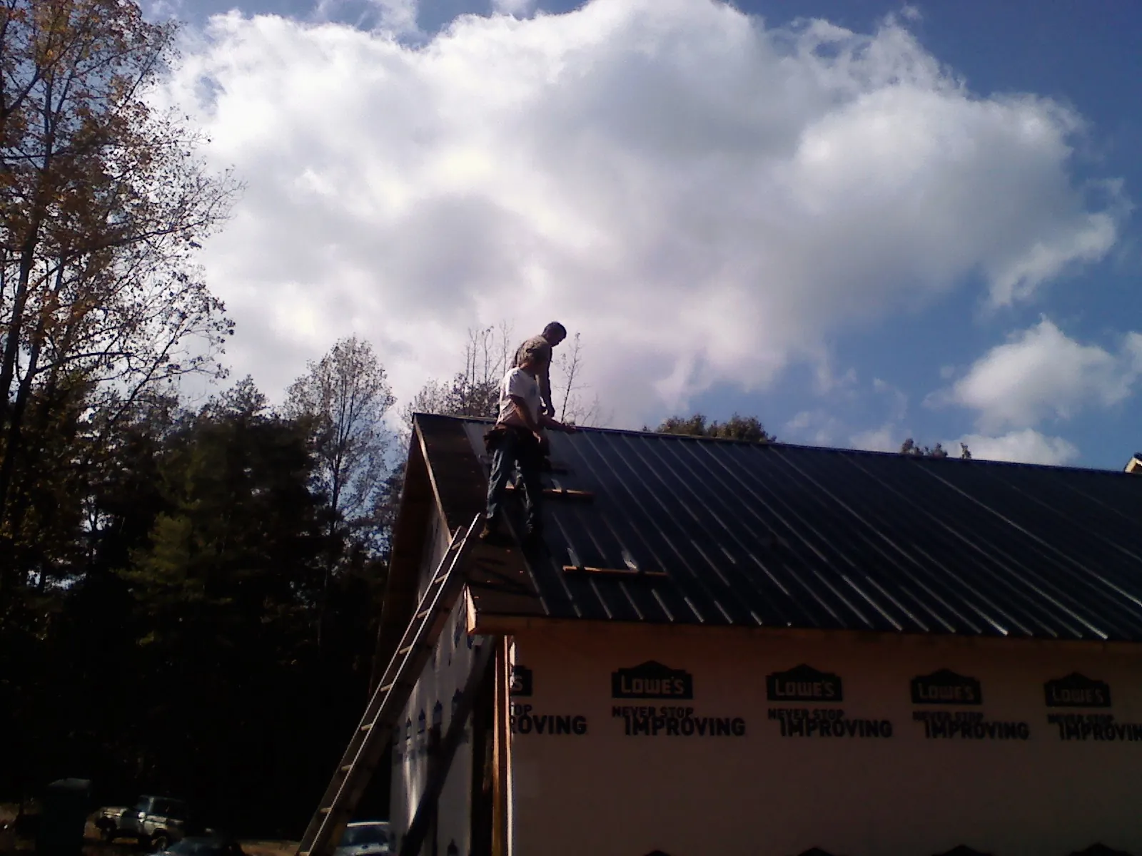 Roofer fastening dark metal panels high against a cloudy sky, from a Roof Inspection job in Bentleyville