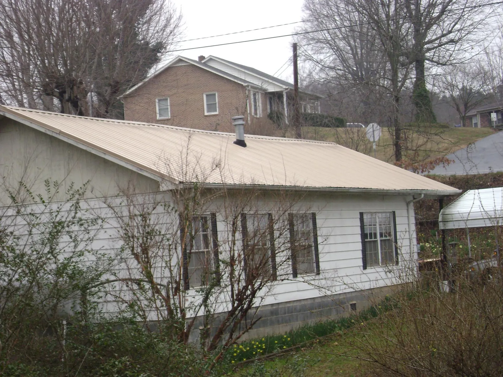 Tan metal roof on a white sided house set into a hillside — Commercial Roofing by Roofing Brothers in Bentleyville