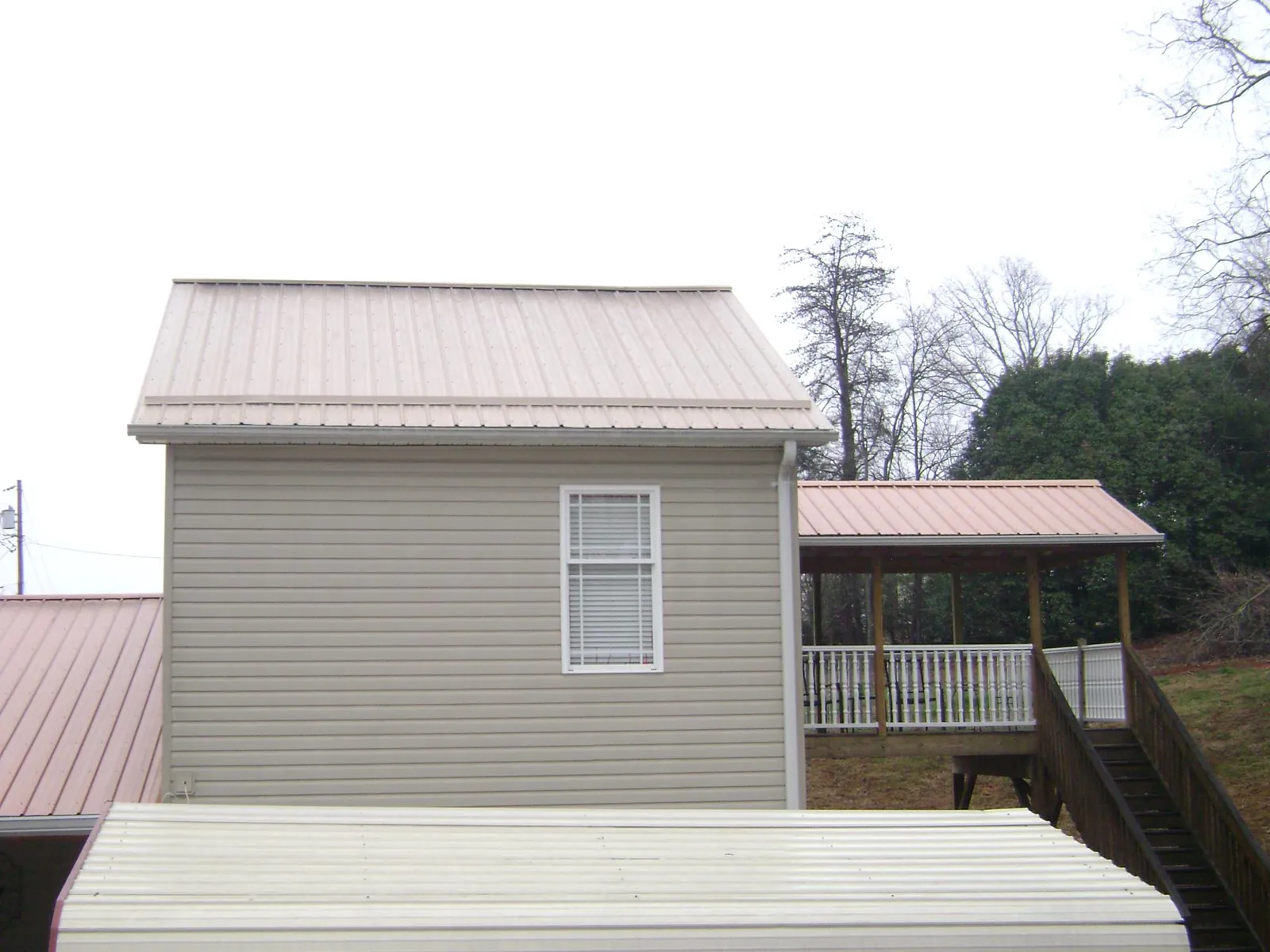 Tan metal roofs on a two story addition and attached porch, from a Roof Replacement job in Bentleyville
